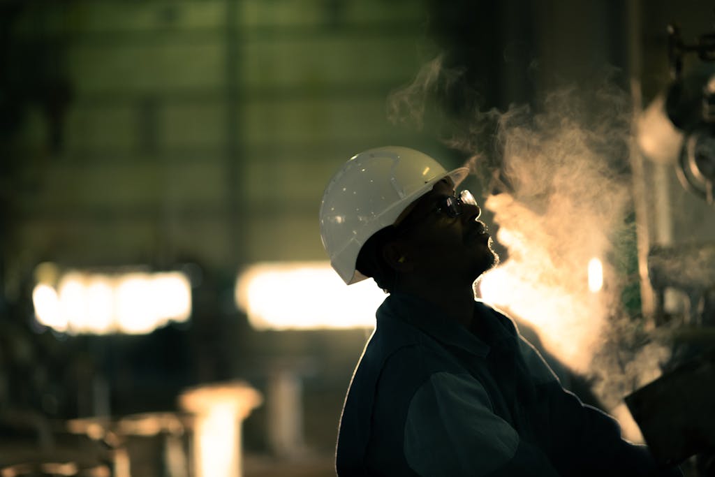 A worker in hard hat surrounded by steam in an industrial setting, conveying energy industry.