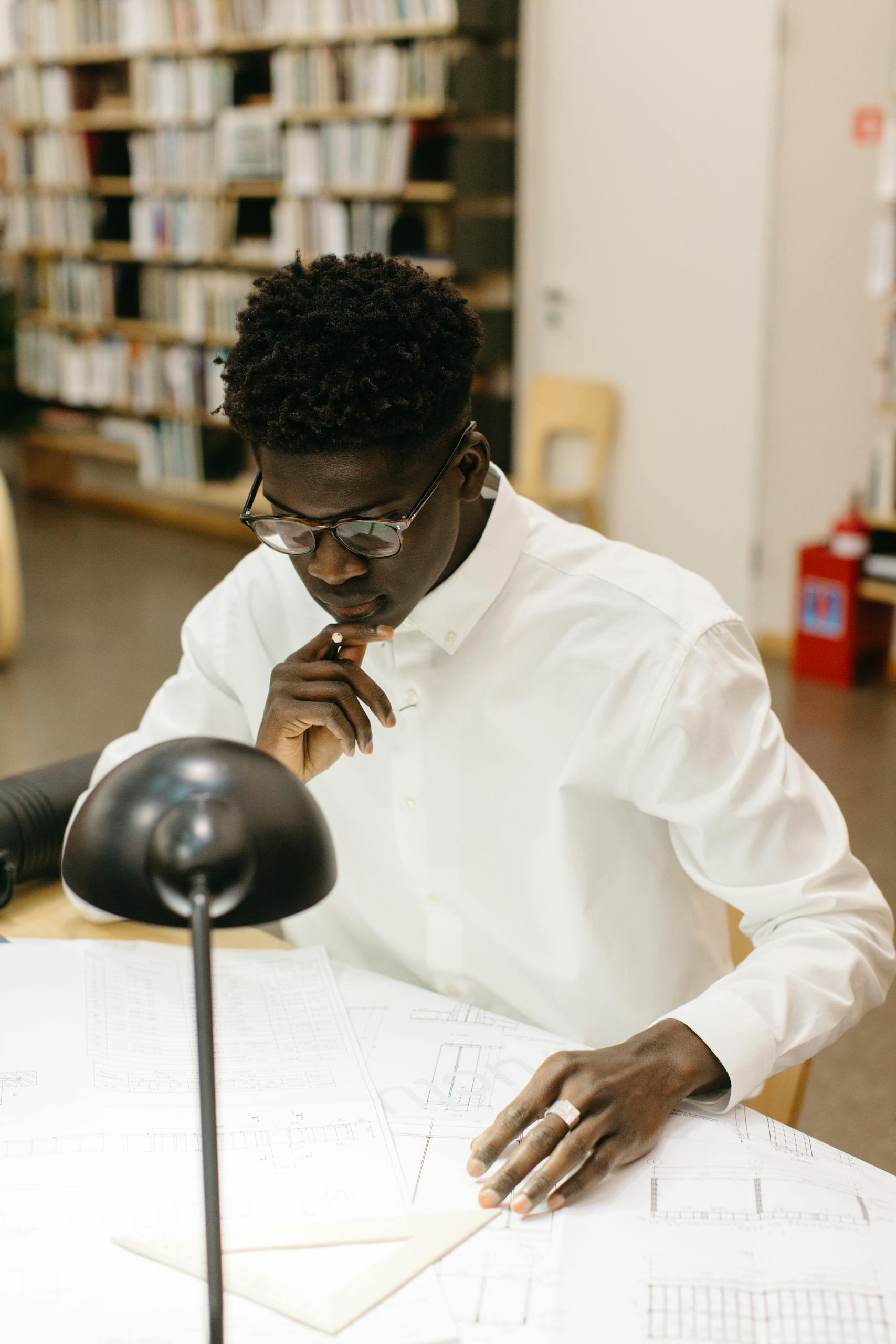 Focused architect in white shirt examining blueprints in a modern office environment.